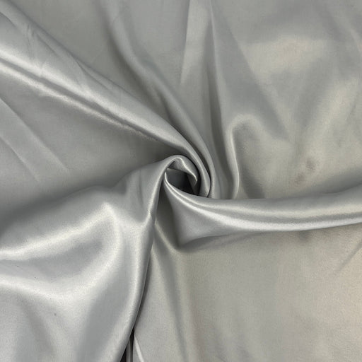 A close-up of draped satin fabric in a light silver-gray color, showing soft folds and a subtle sheen.