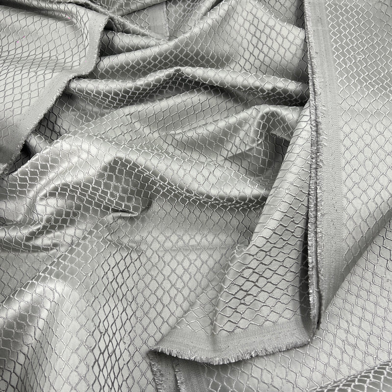 A close-up of draped silver fabric with a woven diamond mesh pattern and a frayed edge.