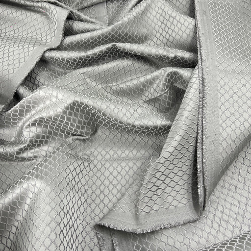 A close-up of draped silver fabric with a woven diamond mesh pattern and a frayed edge.