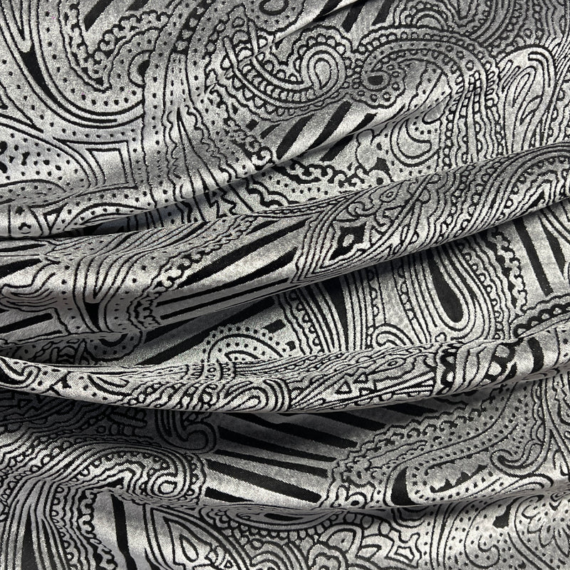 A close-up of draped fabric with an intricate black and silver paisley and abstract line pattern.