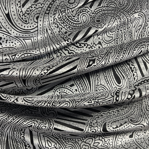 A close-up of draped fabric with an intricate black and silver paisley and abstract line pattern.