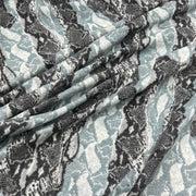 A close-up of draped fabric with a snakeskin pattern in black, gray, and muted blue-gray on a white base.