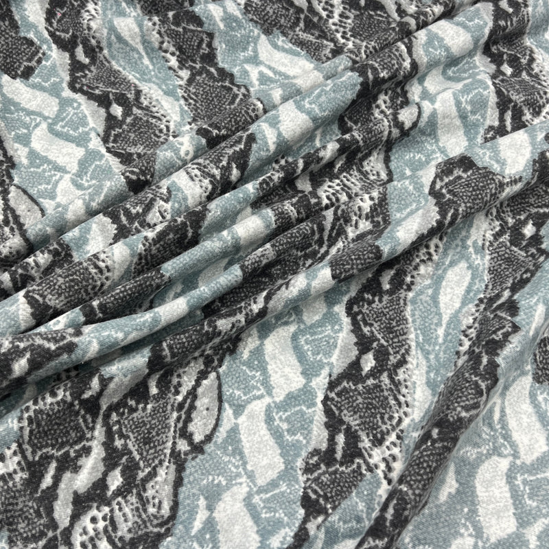 A close-up of draped fabric with a snakeskin pattern in black, gray, and muted blue-gray on a white base.