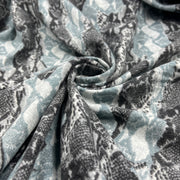 A close-up of draped fabric with a snakeskin pattern in muted blue-gray, charcoal gray, and off-white, gathered in the center to show the material texture and pattern repeat.