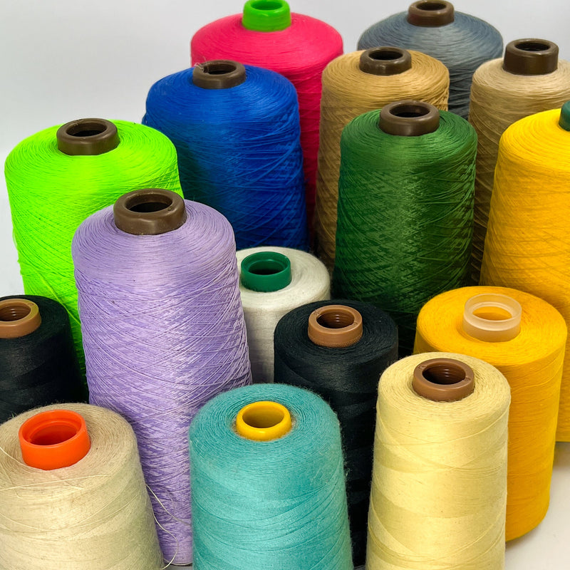 A collection of colorful spools of thread or yarn arranged together on a white background, showing a variety of colors including green, blue, purple, yellow, black, and beige.