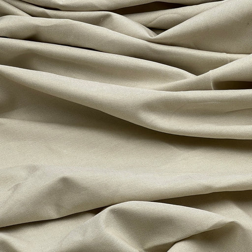 A close-up of draped beige fabric with soft folds and a fine woven texture.
