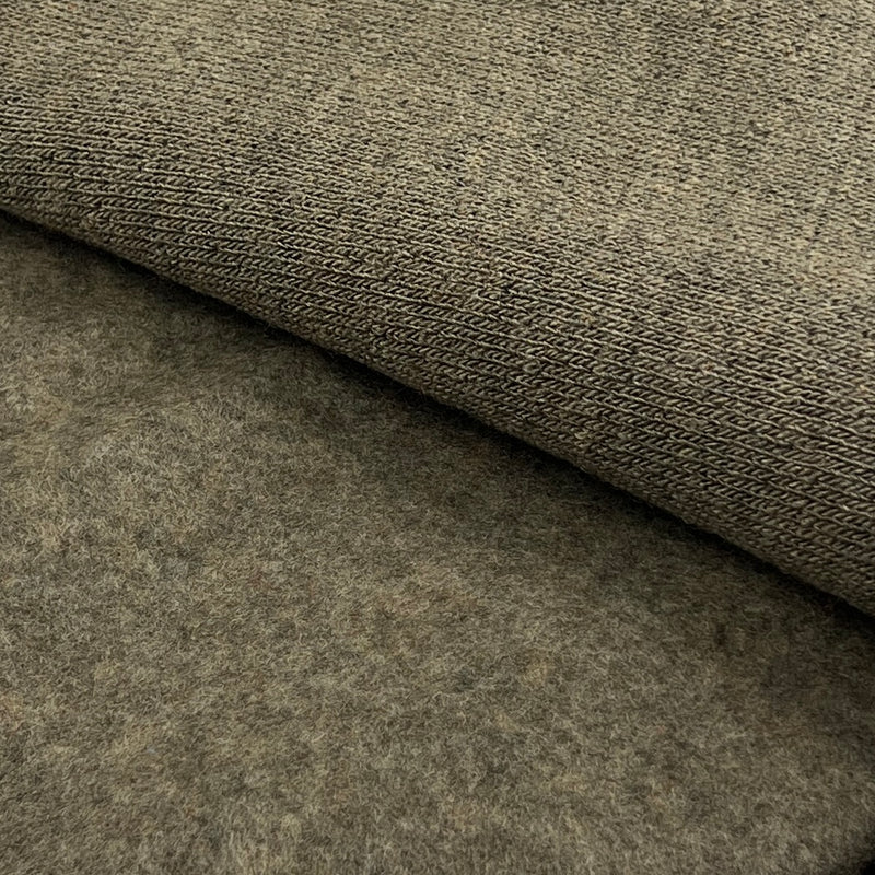 A close-up of a textured fabric or felt material in a warm taupe-brown color, with one corner folded over to show the surface texture.