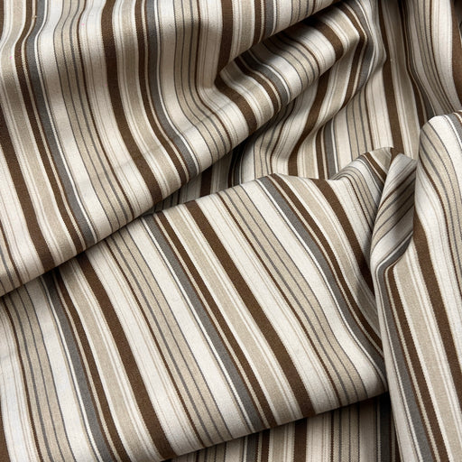 A close-up of draped striped fabric with vertical bands in beige, cream, brown, taupe, and gray.