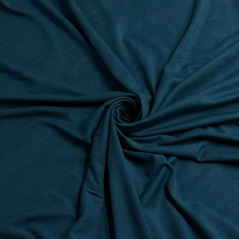 A close-up of dark teal blue fabric arranged in a spiral drape, showing the material's texture and color.