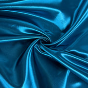 A close-up of shiny blue fabric arranged in a spiral drape, showing a smooth satin-like sheen and folds.