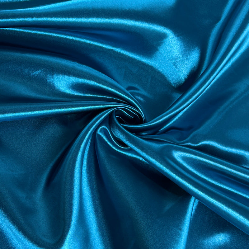 A close-up of shiny blue fabric arranged in a spiral drape, showing a smooth satin-like sheen and folds.