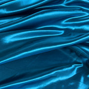 A close-up of draped teal blue satin fabric with a glossy, shiny texture and soft folds.