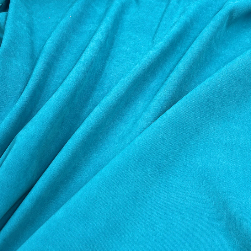 A close-up of draped turquoise blue fabric with soft folds and a smooth matte texture.