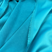 A close-up of bright turquoise blue fabric with a satin-like sheen and visible frayed edges along a seam.
