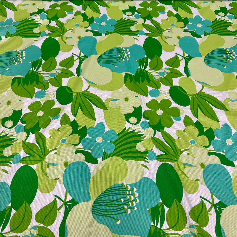 A close-up of a retro floral fabric pattern featuring large teal and light green flowers with dark and light green leaves on a white background.