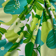 A close-up of draped fabric with a bold retro floral print in green, teal, and light yellow on a white background.