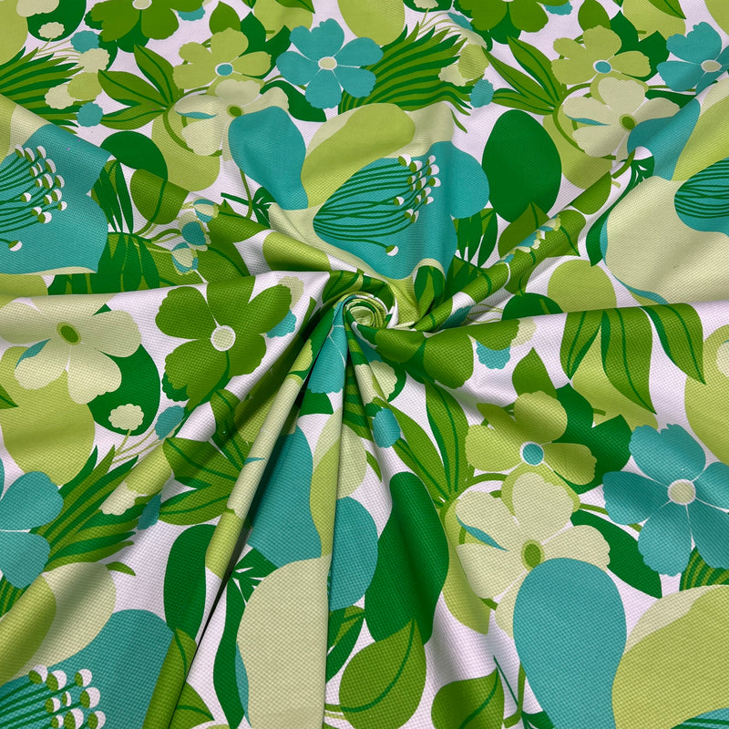 A close-up of a fabric with a retro 1970s floral pattern featuring green, teal, and light yellow flowers on a white background, gathered in the center to show its drape and texture.