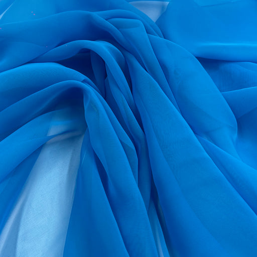 A close-up of draped bright blue sheer fabric with soft folds and a light blue underlying layer visible through the translucent material.