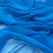 A close-up of draped bright blue sheer fabric with soft folds and a lightweight texture.