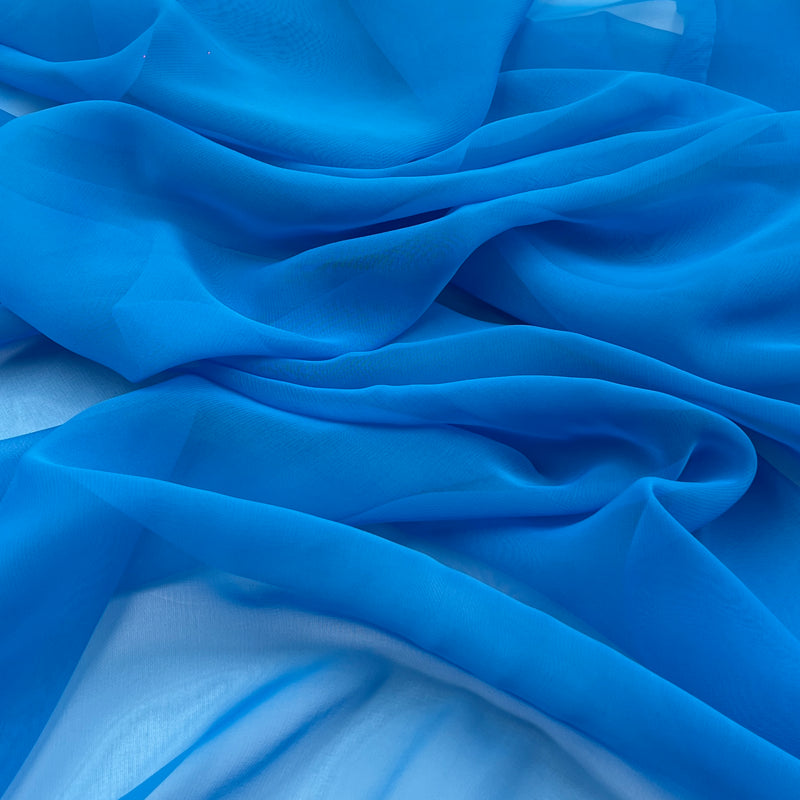 A close-up of draped bright blue sheer fabric with soft folds and a lightweight texture.