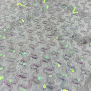 Close-up of a gray textured fabric with raised wavy patterns and scattered iridescent sequins.