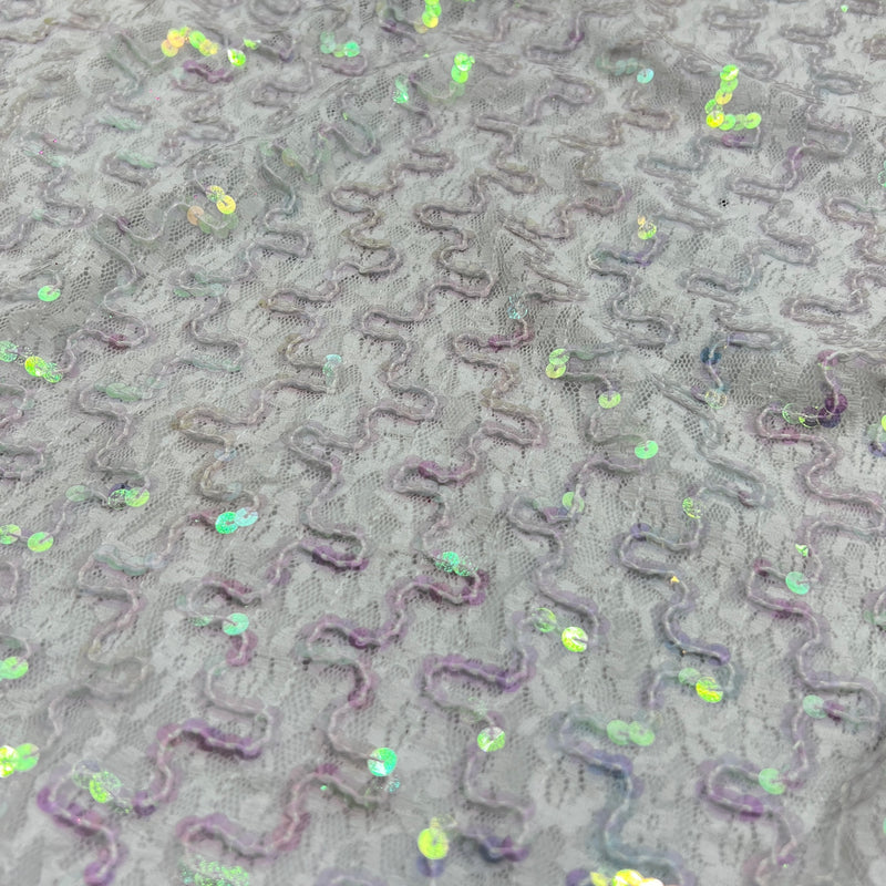 Close-up of a gray textured fabric with raised wavy patterns and scattered iridescent sequins.