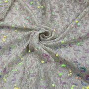 A close-up of a light gray lace fabric with a textured wavy pattern and scattered iridescent sequins, arranged in a spiral drape.