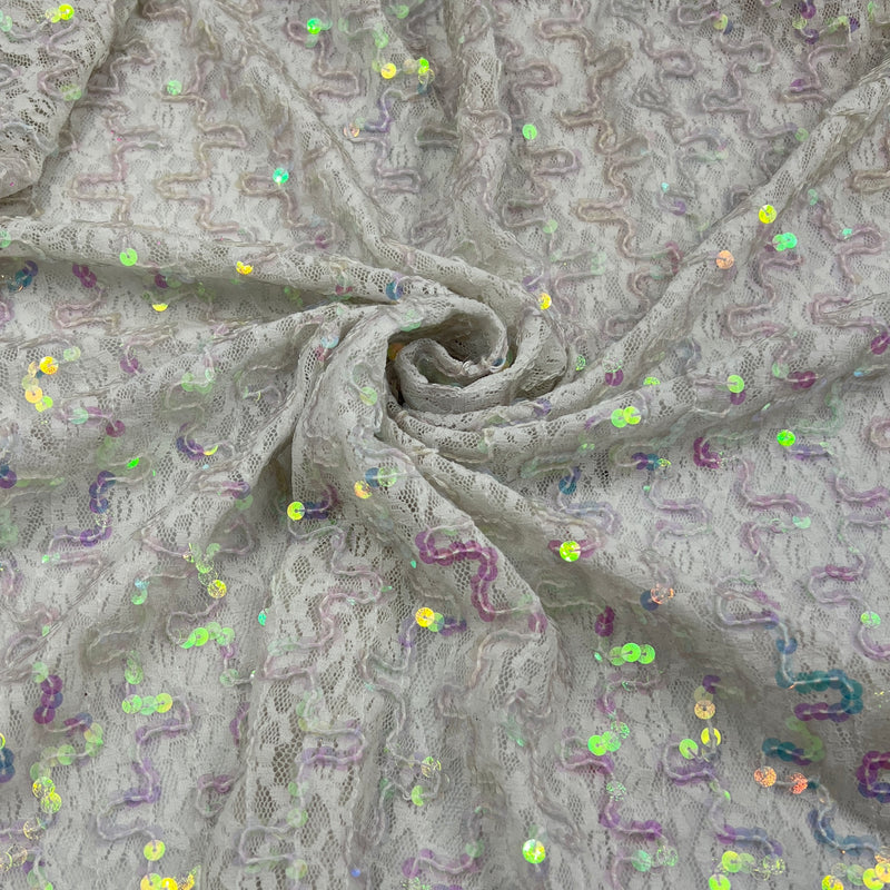 A close-up of a light gray lace fabric with a textured wavy pattern and scattered iridescent sequins, arranged in a spiral drape.