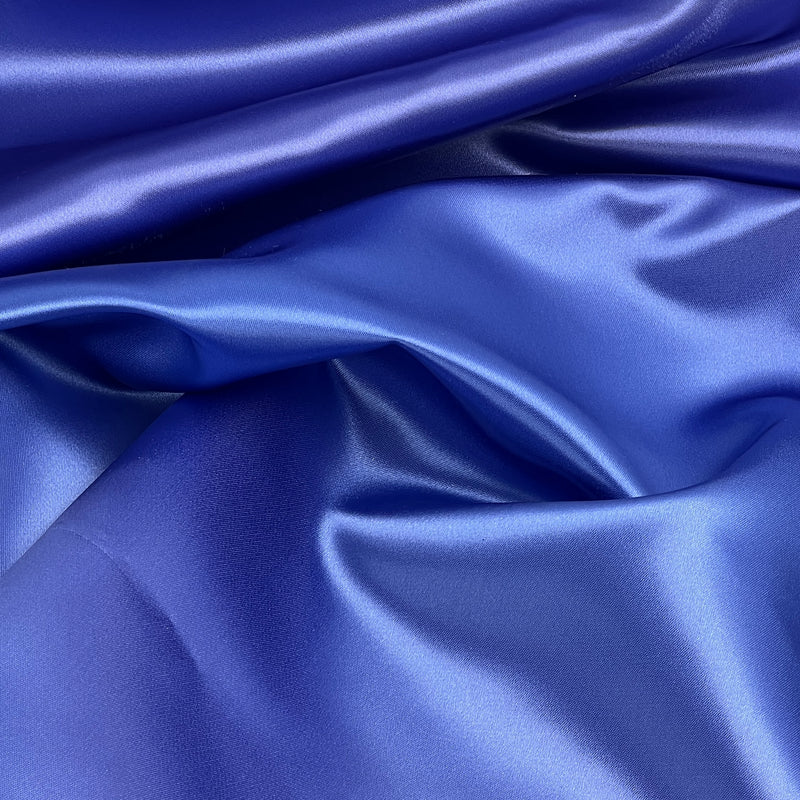 A close-up of draped royal blue satin fabric with a smooth, glossy texture and soft folds.