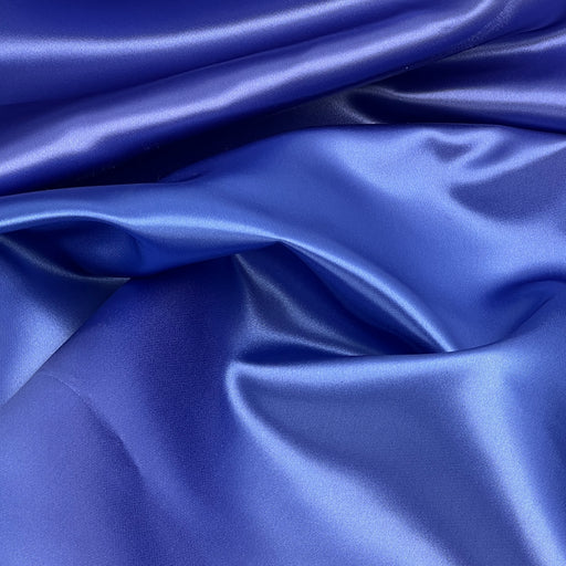 A close-up of draped royal blue satin fabric with a smooth, glossy texture and soft folds.