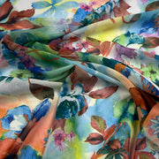 A close-up of draped fabric featuring a vibrant watercolor floral print with blue, green, pink, orange, and brown botanical motifs on a light background.