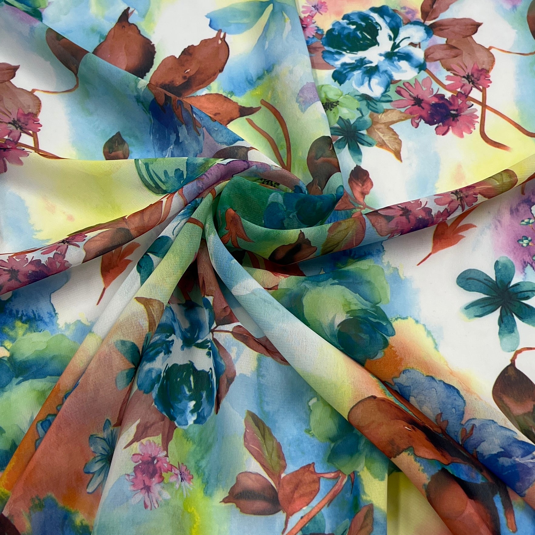 A close-up of a lightweight fabric with a watercolor floral print, draped and twisted to show its soft texture and pattern. The print features blue, green, brown, and pink watercolor flowers and leaves on a white background.