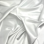A close-up of draped white satin fabric with soft folds and a subtle sheen.