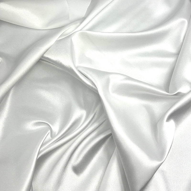 A close-up of draped white satin fabric with soft folds and a subtle sheen.