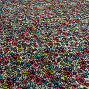 Close-up of a cotton fabric with a dense, small-scale floral print featuring pink, blue, yellow, and white flowers outlined in black.