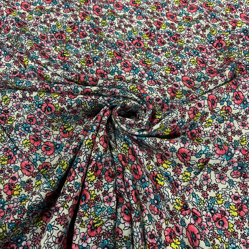 A close-up of a lightweight fabric with a dense, all-over floral print. The pattern features pink and red flowers, teal and blue blossoms, and small yellow accents on a white background, styled with a central swirl to show the material's drape and texture.