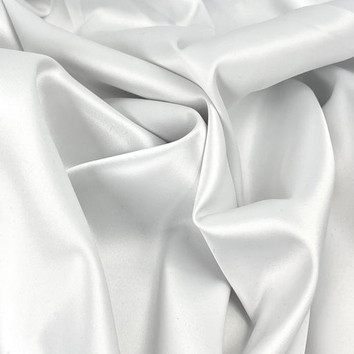 Closeup of satin twill woven fabric with a subtle sheen and smooth, elegant drape. Bunched into a pile, showing off the smooth, silky hand.