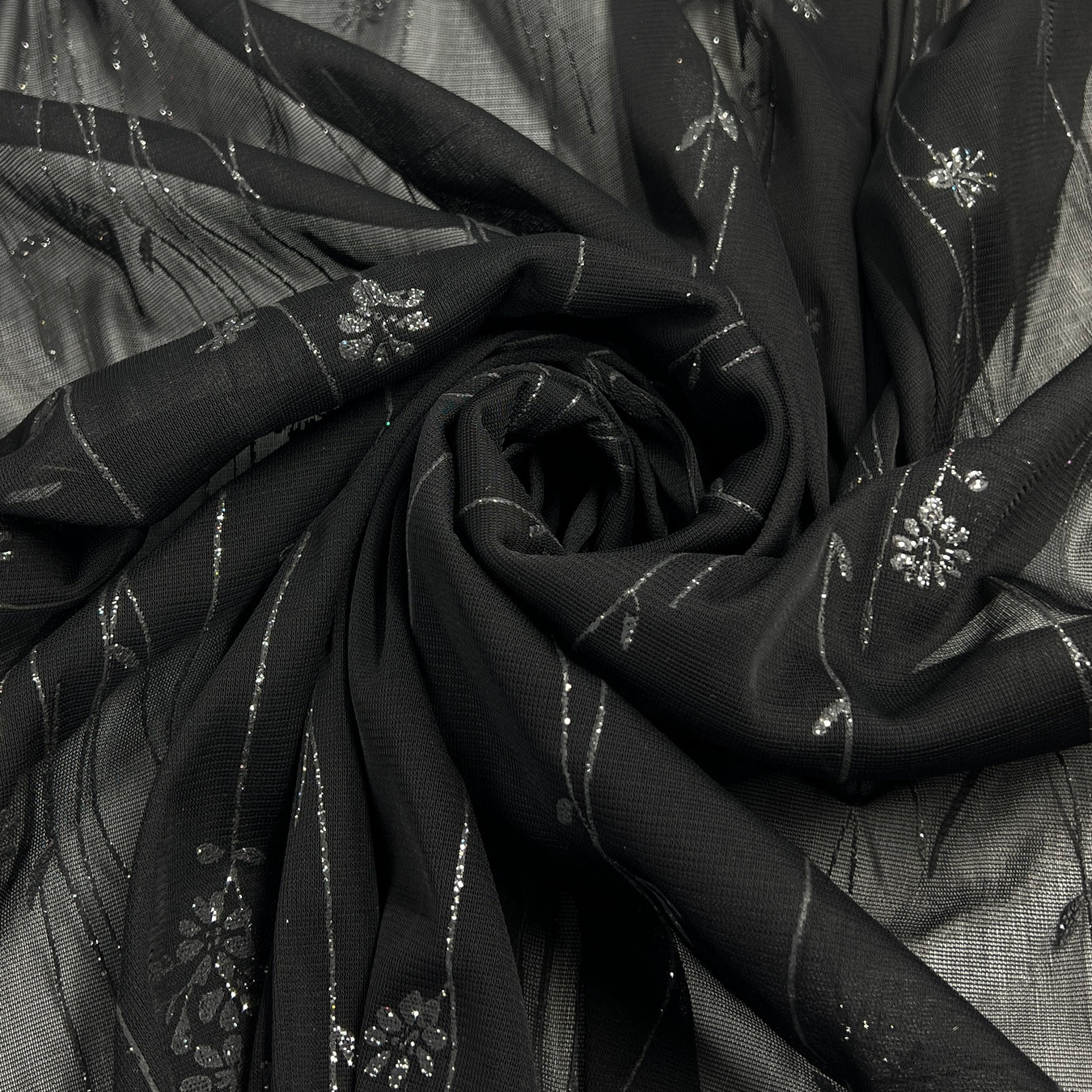 Black sheer fabric with silver floral glitter design and metallic stripes, arranged in a spiral drape.
