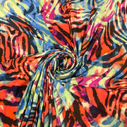 A vibrant multicolor fabric with a bold abstract pattern of zebra stripes and watercolor splashes in orange, pink, blue, yellow, green, and black, styled in a central spiral drape.